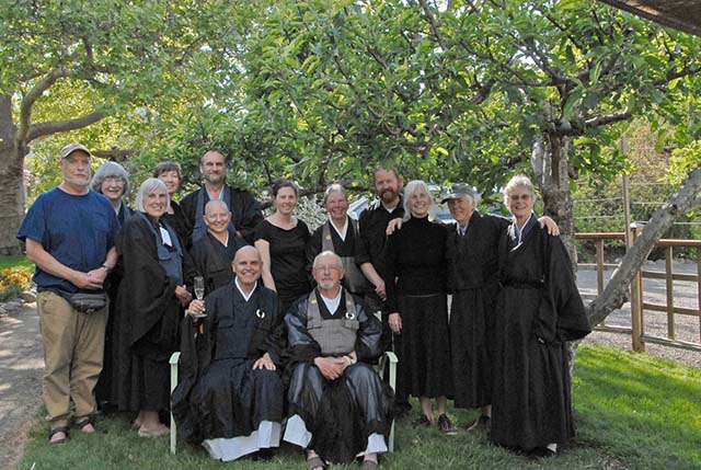 Abbot Jintei Harold Little (with puppy Koda in his arms) and Abbess Etsudo Patty Krahl (holding basket), surrounded by the Ashland Zen Center sangha on the steps of the dining hall porch, while it was still under construction