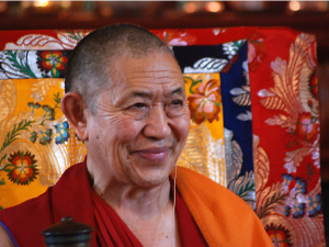 Garchen Rinpoche smiling at students and turning his prayer wheel, which he spins continuously.