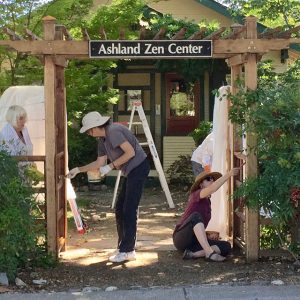 Sangha hands keep the facility in good repair. In 2016, members apply a fresh coat of stain to the entry gate.