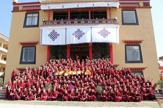 Group shot of the 10 geshema graduates, holding their yellow hats, on the steps of Kopan Nunnery in Nepal