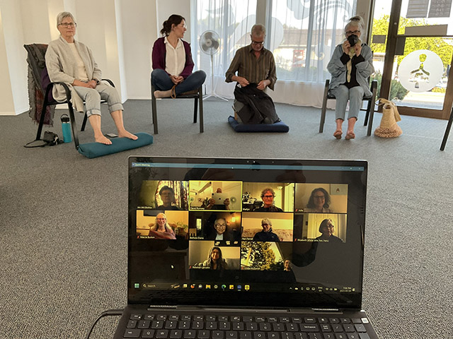 Sangha member gather both online and in-person at the Salt Spring Insight Meditation community. The laptop get passed around the room at the beginning of the session so that members can greet each other