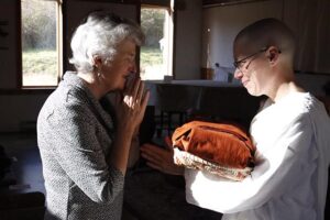 Dharma teacher Kate Davies offers the robes to Anagārikā Bethany