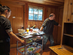 Cooks Sihan Lin and Brock Brown prepare to roll the food cart into the sala to offer the meal Ajaan Peter and Taan Will