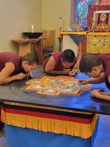 Midway through the build, Chung Dolma (left), Sonam Dolma (middle), and Sherab Dolma (right), use chak-purs to coax grains of colored sand into their rightful places inside the mandala