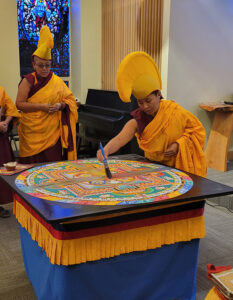 Sonam Dolma performs the dissolution of the sand mandala, dragging a large paint brush through the design until all that remains is a mound of colored dust